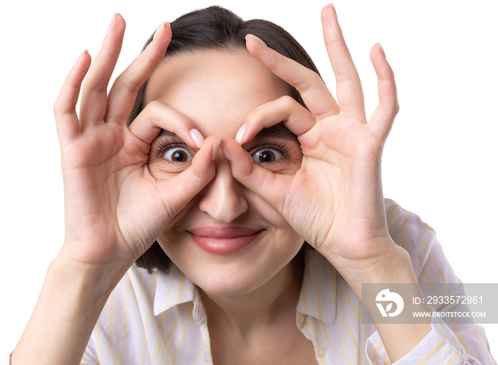 Close up portrait of attractive quirky young woman making binoculars with hands showing ok gesture on white studio background.