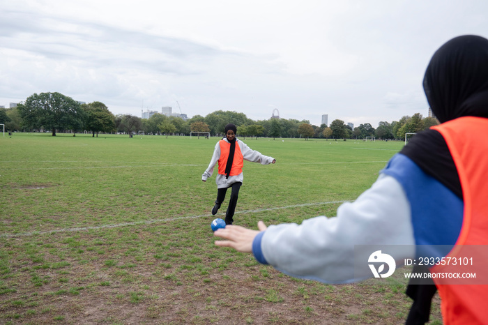 Two women in hijabs playing soccer in park