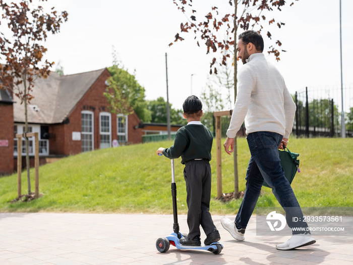 Boy (6-7) on push scooter walking with father to school