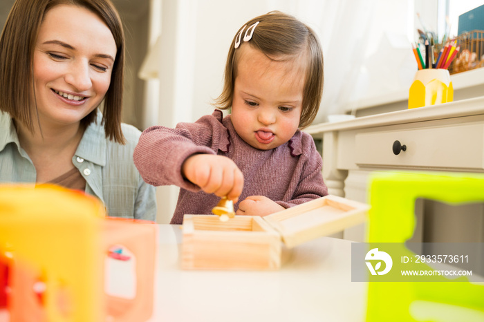 Woman playing with her little daughter with down syndrome at the table