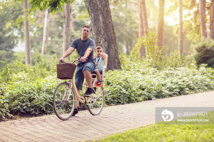 father and son riding a bicycle together outdoors in a city park.