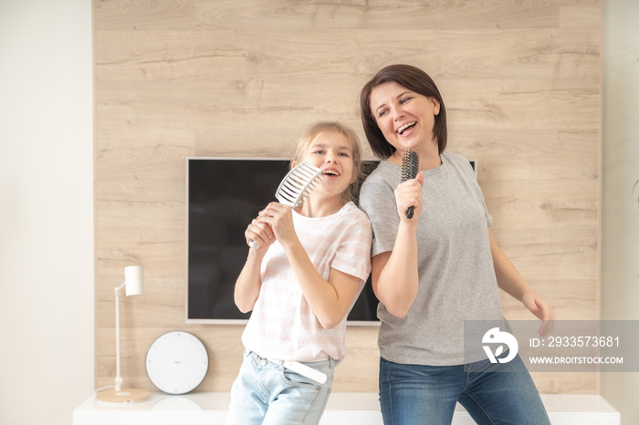 Happy family young adult mother and cute teen daughter having fun singing karaoke song in hairbrushes. mother laughing enjoying funny lifestyle activity with teenage girl at home together.