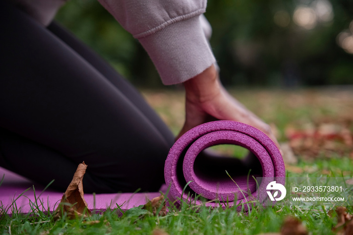 Close-up of woman rolling up yoga mat on grass in park