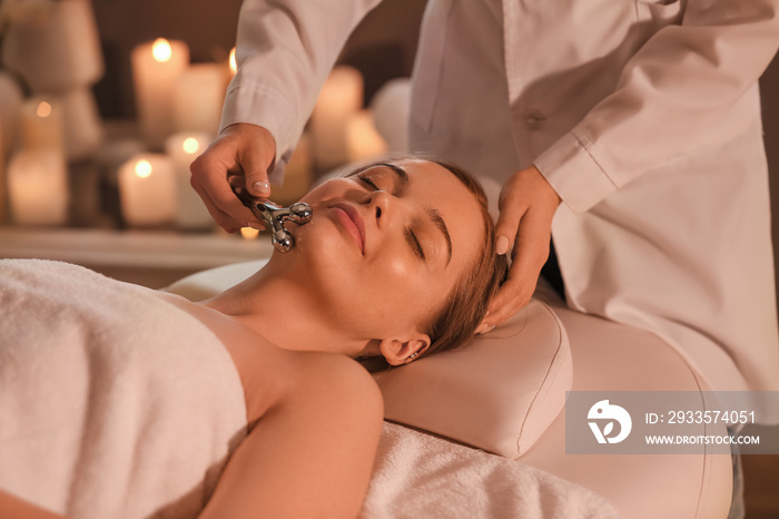 Pretty young woman receiving face massage with roller in beauty salon