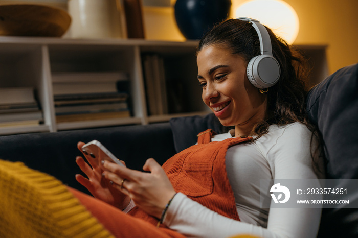 Side view of a young woman relaxing at home with her phone