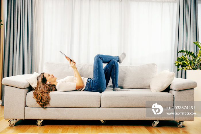 A happy woman relaxing with technologies at her home.