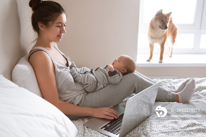 Busy young woman working or study on laptop computer while holding her baby in arms at home