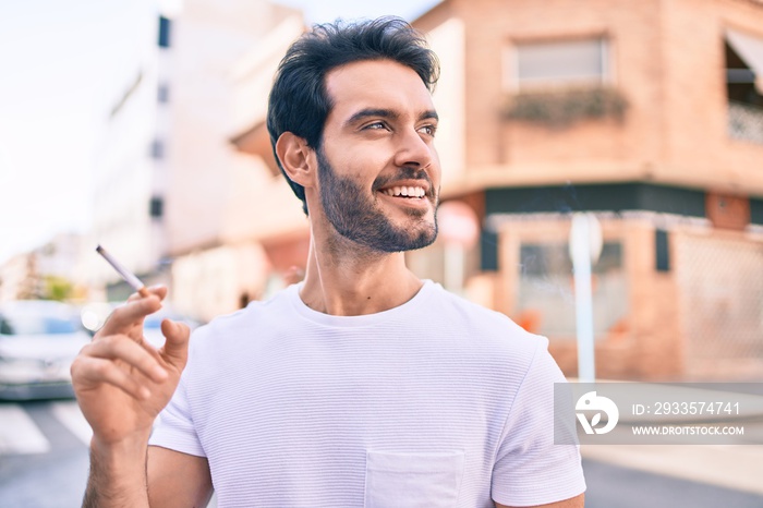 Young hispanic man smiling happy holding cigarette walking at the city.