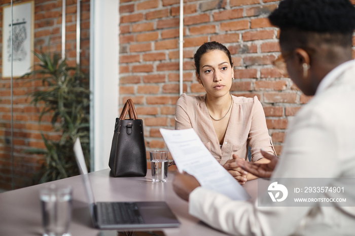 Young woman talks to member of human resource team while applying for job in office.