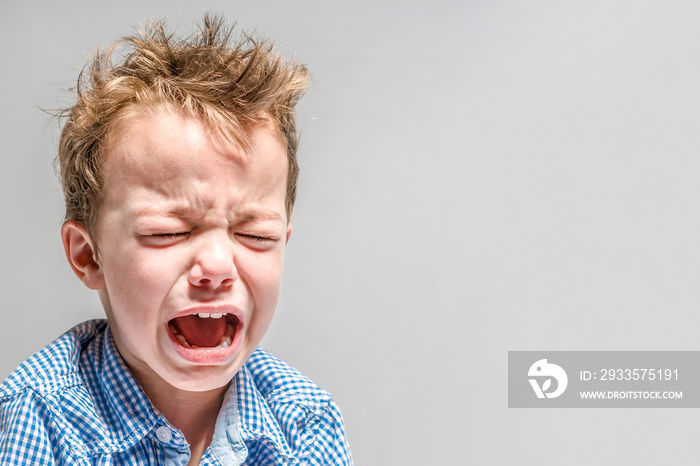 Crying little boy on a gray background .