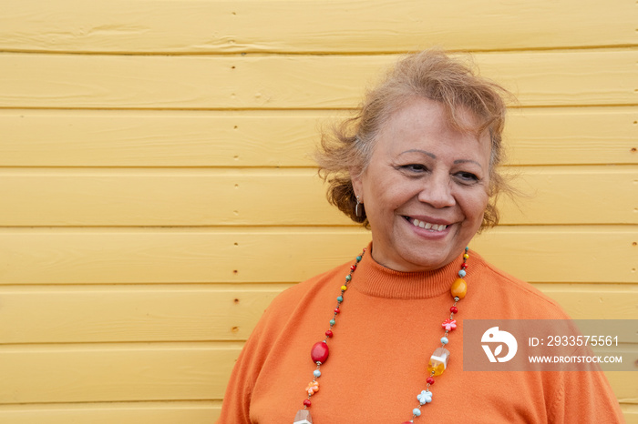 Portrait of smiling senior woman against yellow wall