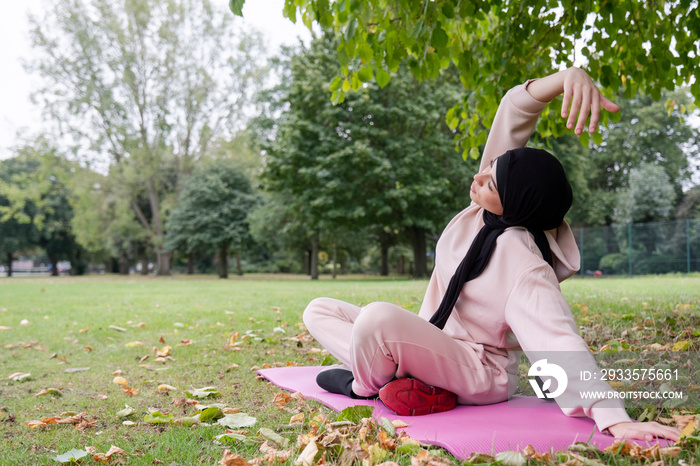 Woman in hijab and pink tracksuit stretching in park