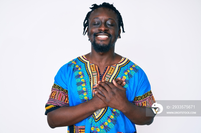 Young african american man with braids wearing traditional africa tshirt smiling with hands on chest with closed eyes and grateful gesture on face. health concept.