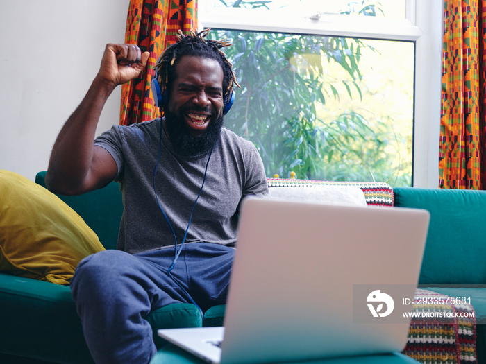 Man lying on sofa, listening to music from laptop