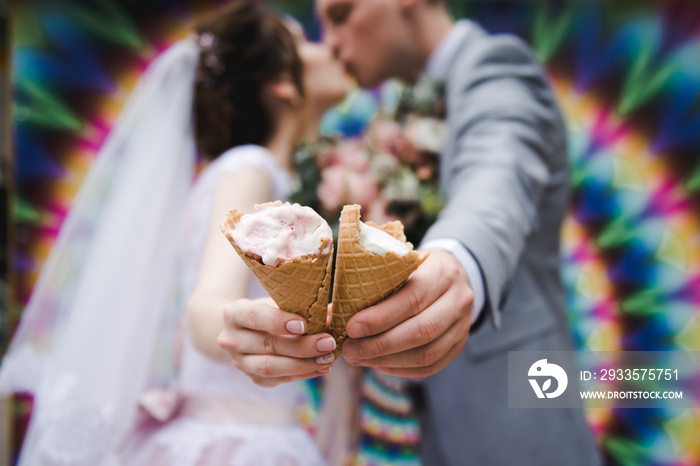 The bride and groom are eating ice cream together on a bright wall background. Funny newlyweds eat ice-cream. Happy Wedding Day