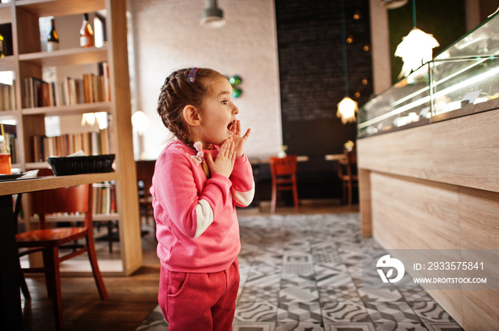 Young girl wth shocked reaction in cafe choose a dessert from shop window.