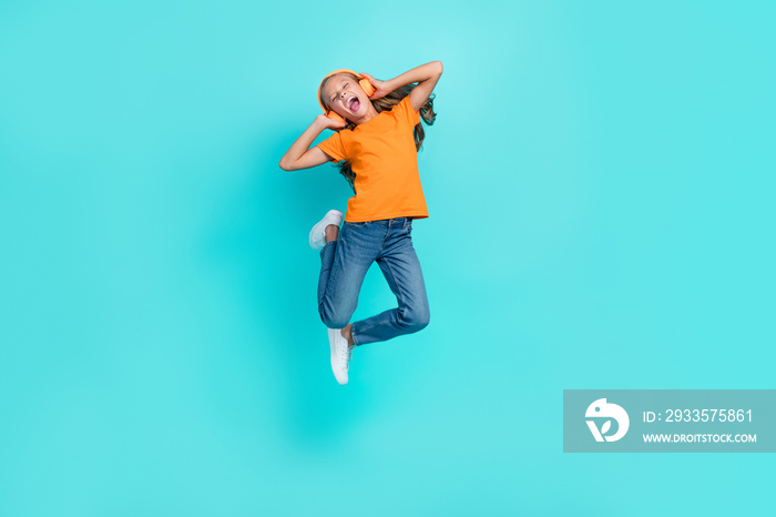 Full length photo of cool cheerful little child dressed orange t-shirt jumping high enjoying music isolated teal color background