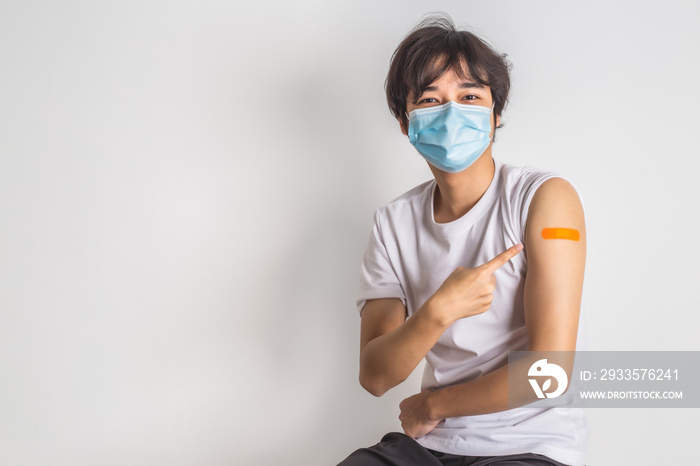 Asian man wearing face mask with a smile on his face showing his vaccinated arm. vaccination, recommended inoculation concept.