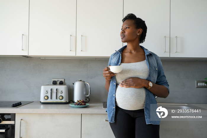 Pregnant woman holding tea cup in kitchen