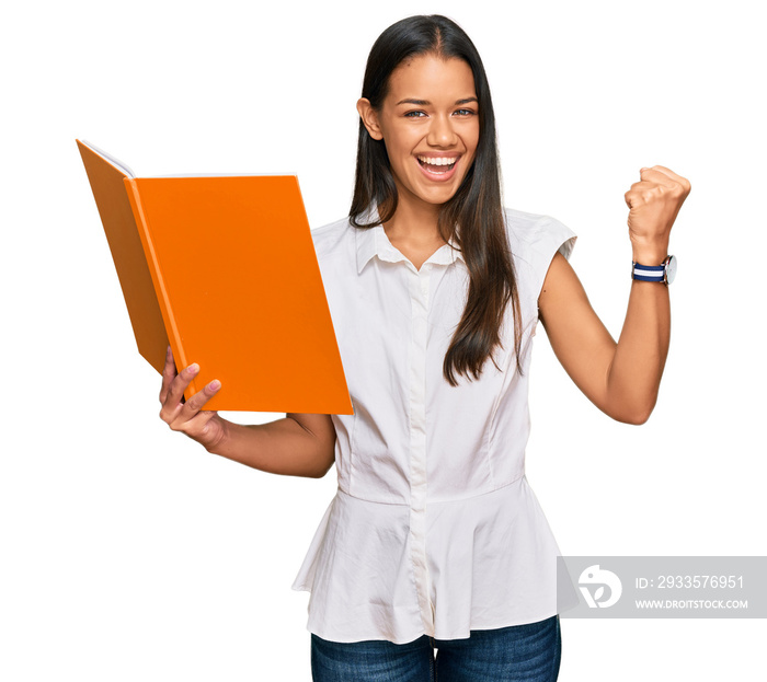 Beautiful hispanic woman reading book screaming proud, celebrating victory and success very excited with raised arms