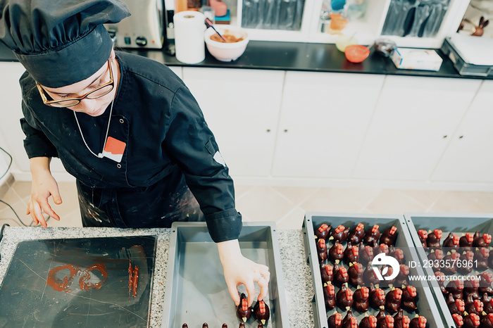 high angle view of female chocolatier in chef uniform working on pastry in the kitchen