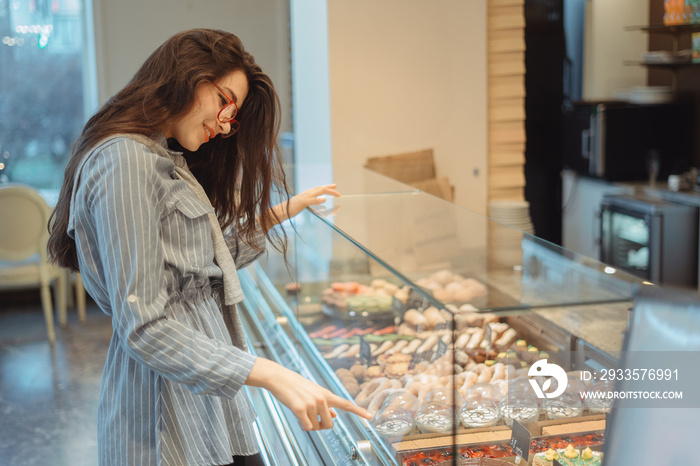 A beautiful young asian girl with long hair chooses a dessert in a cafe by the window. Beautiful interior of bakery cafe