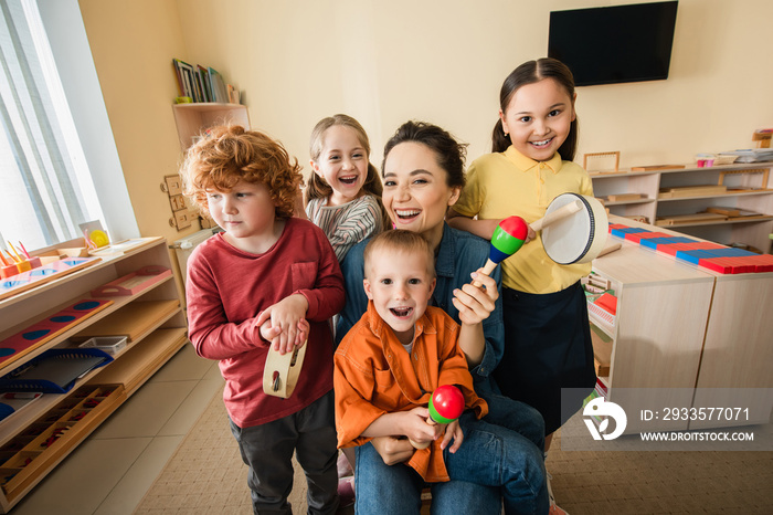 happy teacher with interracial kids playing musical instruments in montessori school