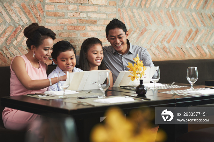 Smiling Vietnamese family reading menu at restaurant