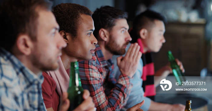 Group of funny male friends multi-ethnic men football fans gathering at night together watching soccer gameplay competition match on TV.