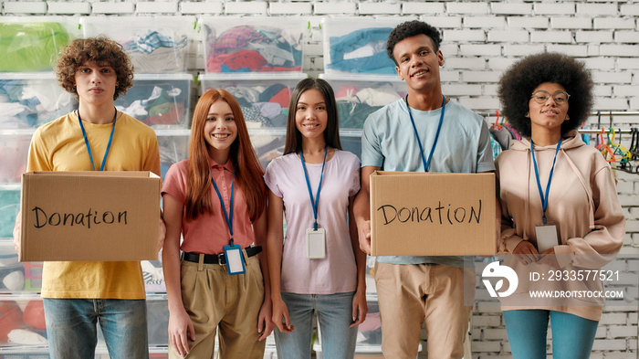 Young diverse volunteer group smiling at camera, holding donation boxes, Happy team working for a charity, donating apparel to needy people