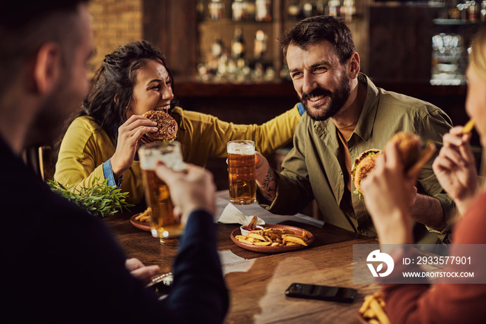 Group of happy friends having fun while drinking beer and eating hamburgers in a pub.