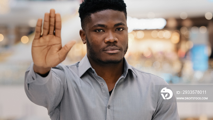 Close-up of young serious confident african american man looking at camera puts forward palm showing stop gesture demonstrating protection personal boundaries protest against violence racism refusal