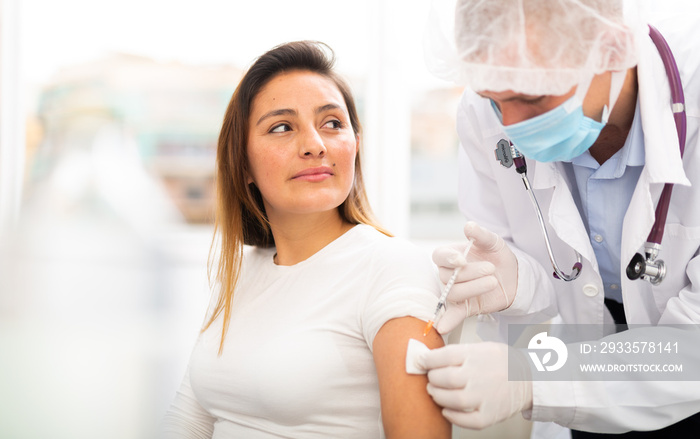 Doctor male giving Covid-19 or flu antivirus vaccine shot to female patient at health clinic or hospital office