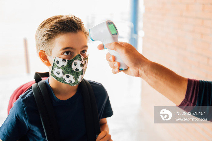 teacher taking a boy temperature with a thermometer during covid pandemic.