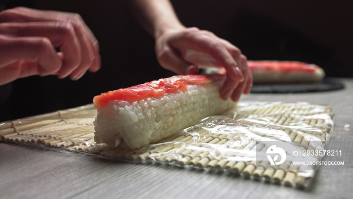 Cropped anonymous cook hands with rolling fresh sushi with bamboo mat while working in authentic Japanese restaurant,Close-up of chef’s hands rolling a sushi roll on bamboo mat.Sushi making process