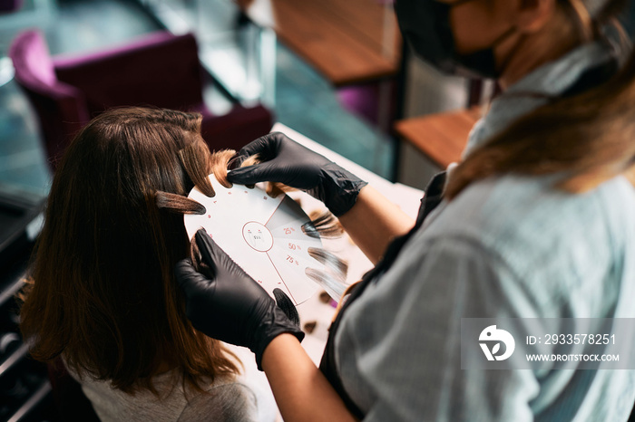 Close-up of hairdresser chooses shade of hair color while having appointment with female customer at the salon.