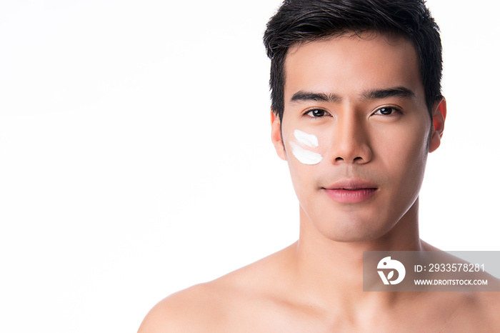 Portrait of young handsome man applying cream lotion on face, isolated on white background