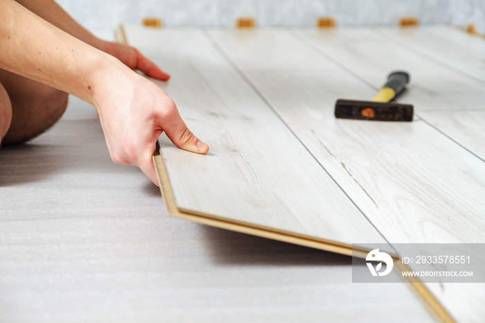 male hands is laying wooden panel of laminate floor indoors closeup. Laminate flooring, selective focus