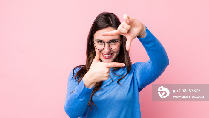 young pretty woman feeling happy, friendly and positive, smiling and making a portrait or photo frame with hands