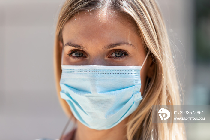 Beautiful blonde woman wearing protective mask on street.