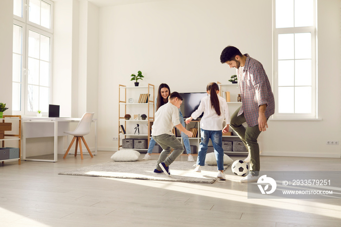 Happy family stay at home. Parents and kids having fun together playing football in living-room. Children attacking father kicking ball, mother on gate. Leisure activity during covid19 quarantine