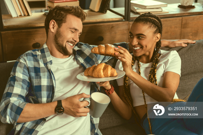 What some bite. Adorable couple spending morning together and smiling while trying on some tasty pastry.