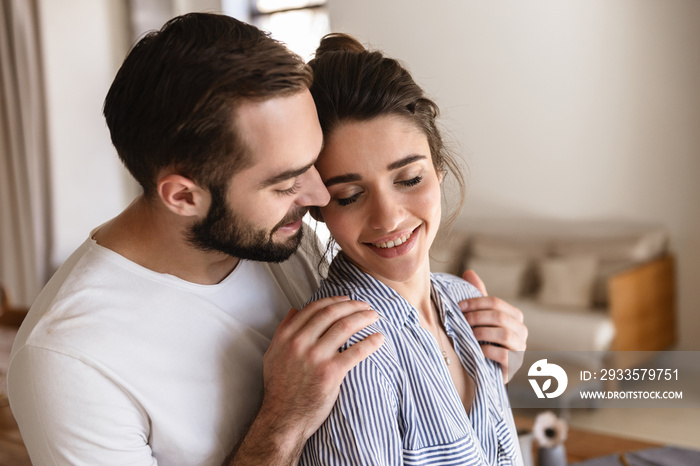 Photo of gentle brunette couple in love smiling while hugging together in apartment