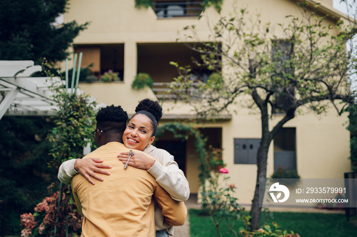 Multiracial couple holding keys and standing outside their new home