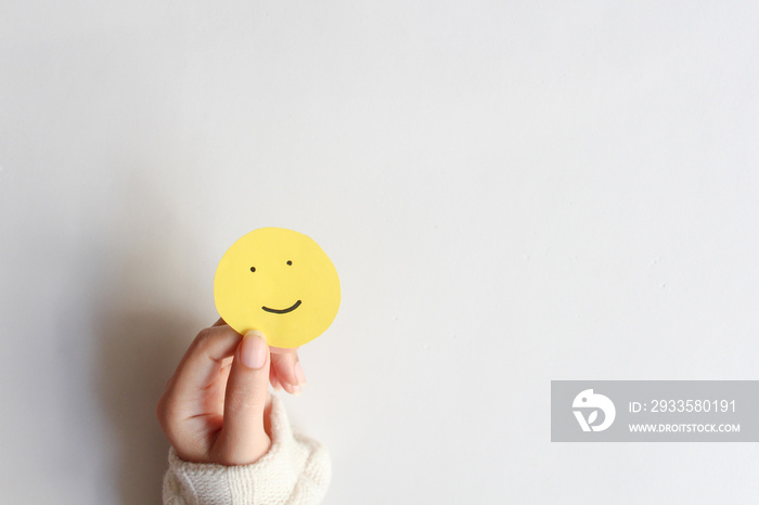 Woman hands holding yellow smile face paper on white background, top view, good feedback rating,think positive, customer review, assessment, world mental health day, Compliment Day.