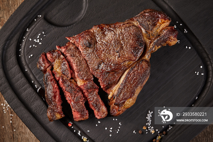 Sliced grilled veal steak with condiments on wooden board