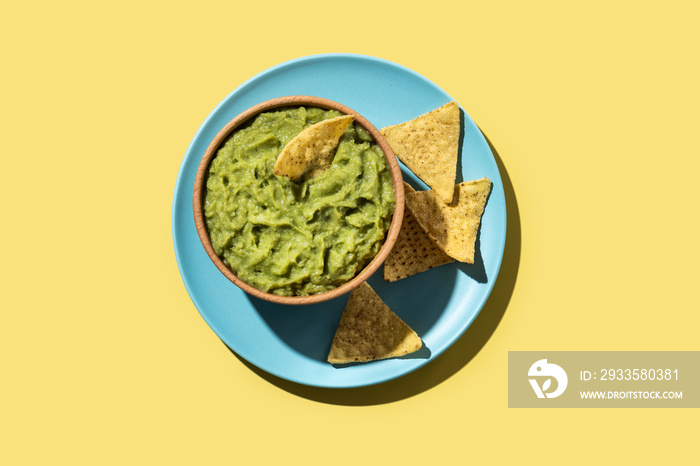 Mexican guacamole with nacho chip in wooden bowl on yellow background. Top view