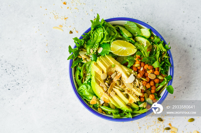 Green healthy salad with avocado, baked chickpeas and seeds in white bowl, top view.