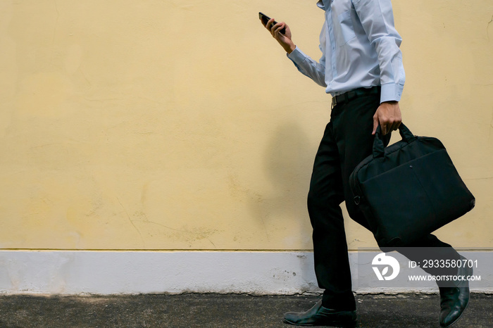 A man in formal outfit holding phone and laptop bag while walking to work