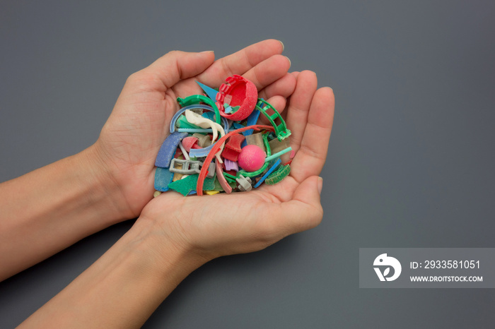 Hands full of microplastics collected on the beach. Plastic pollution concept.